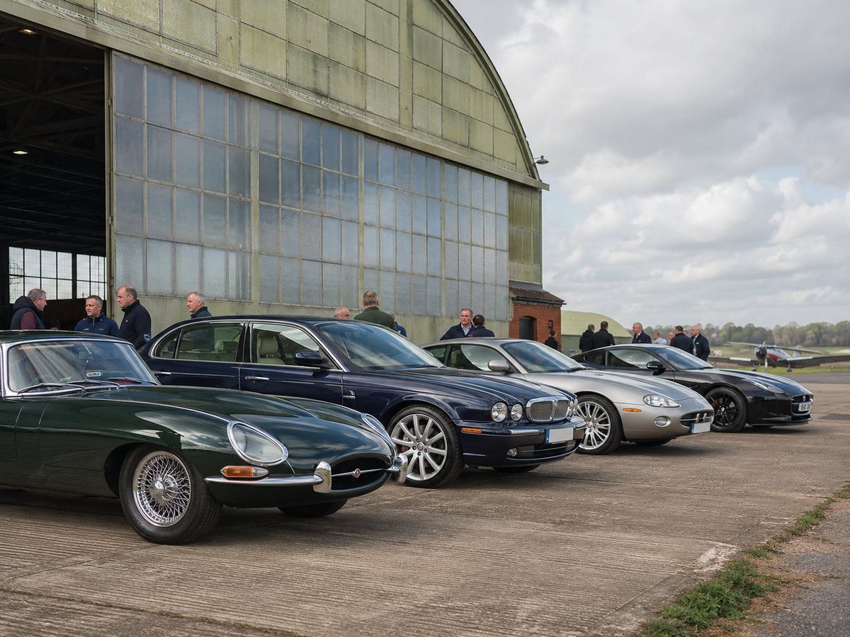 A gathering of Jaguar cars and enthusiasts outside a heritage hangar